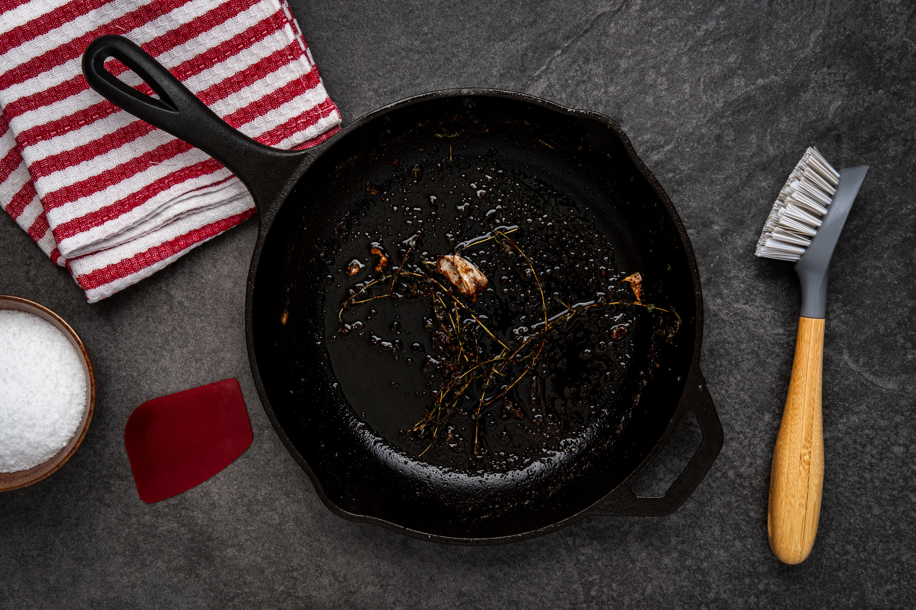 Dirty cast iron skillet next to a cleaning brush