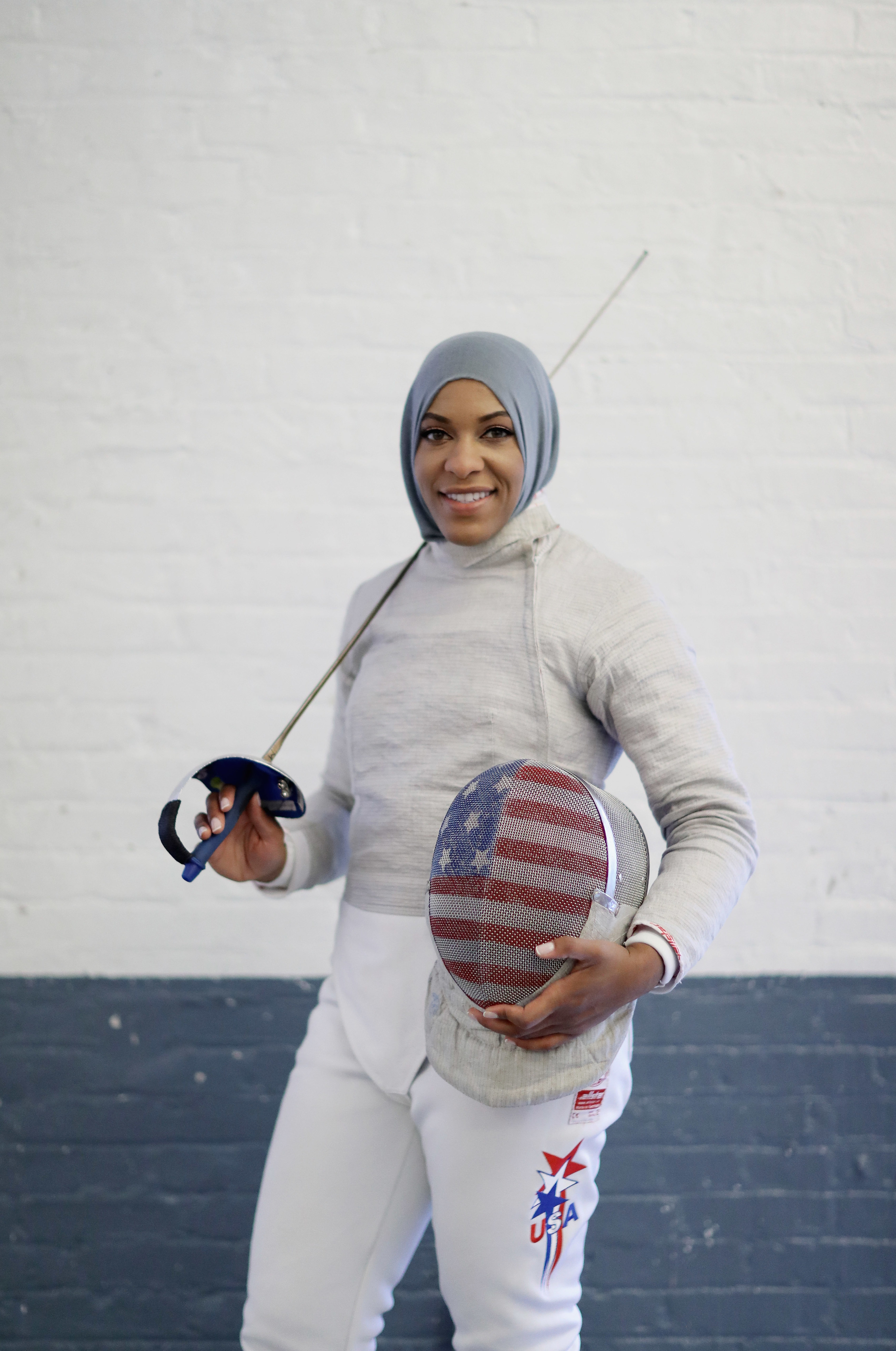 American Olympic fencer Ibtihaj Muhammad poses for a portrait at the Fencers Club. She holds her helmet, which has the U.S. flag printed on the mesh, and her fencing sabre.