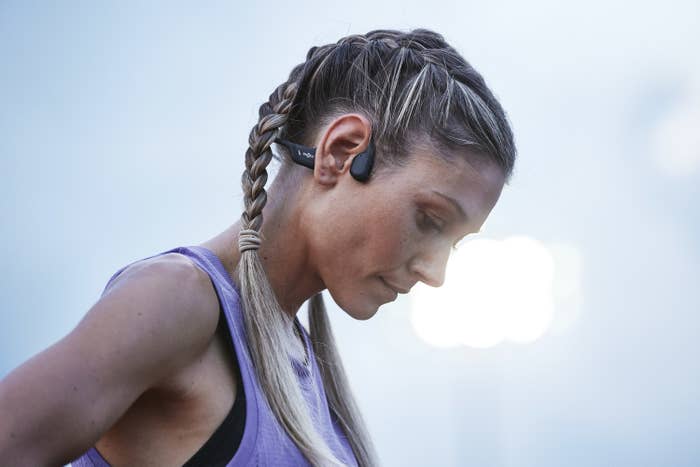 A woman in athletic clothes wearing the open run pro headphones from shokz