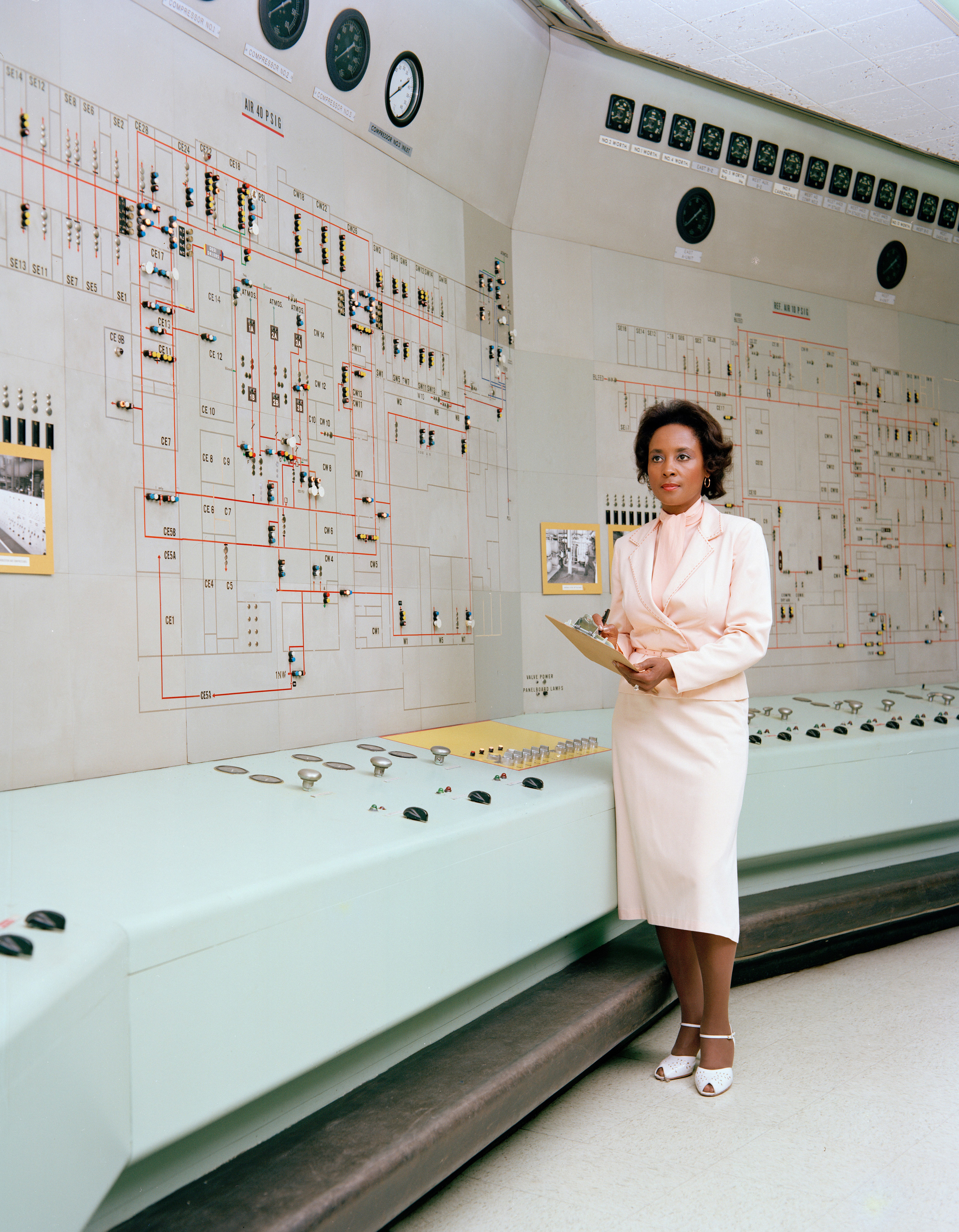 Annie Easley, standing with a clipboard at NASA Lewis Research Center. She wears a fitted three piece suit with a skirt and peeptoe shoes.