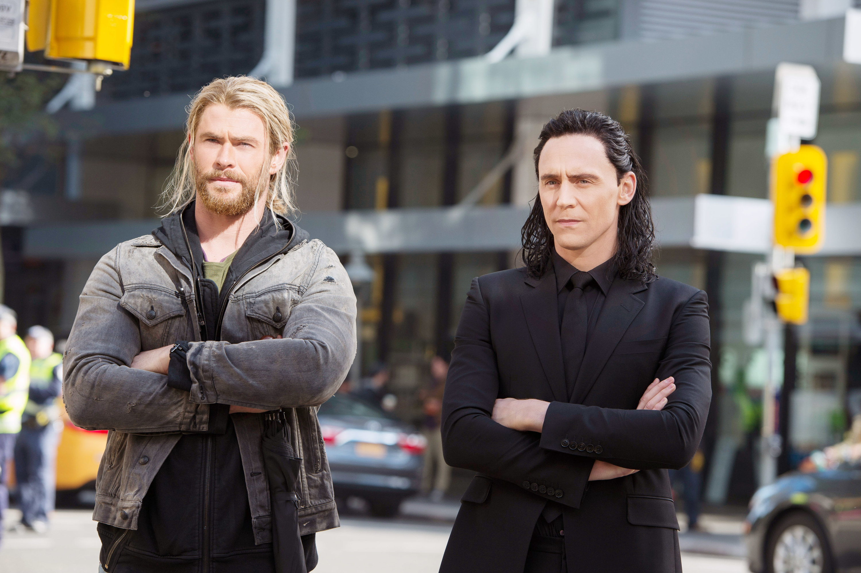 Loki and Thor standing in normal clothes with their arms crossed