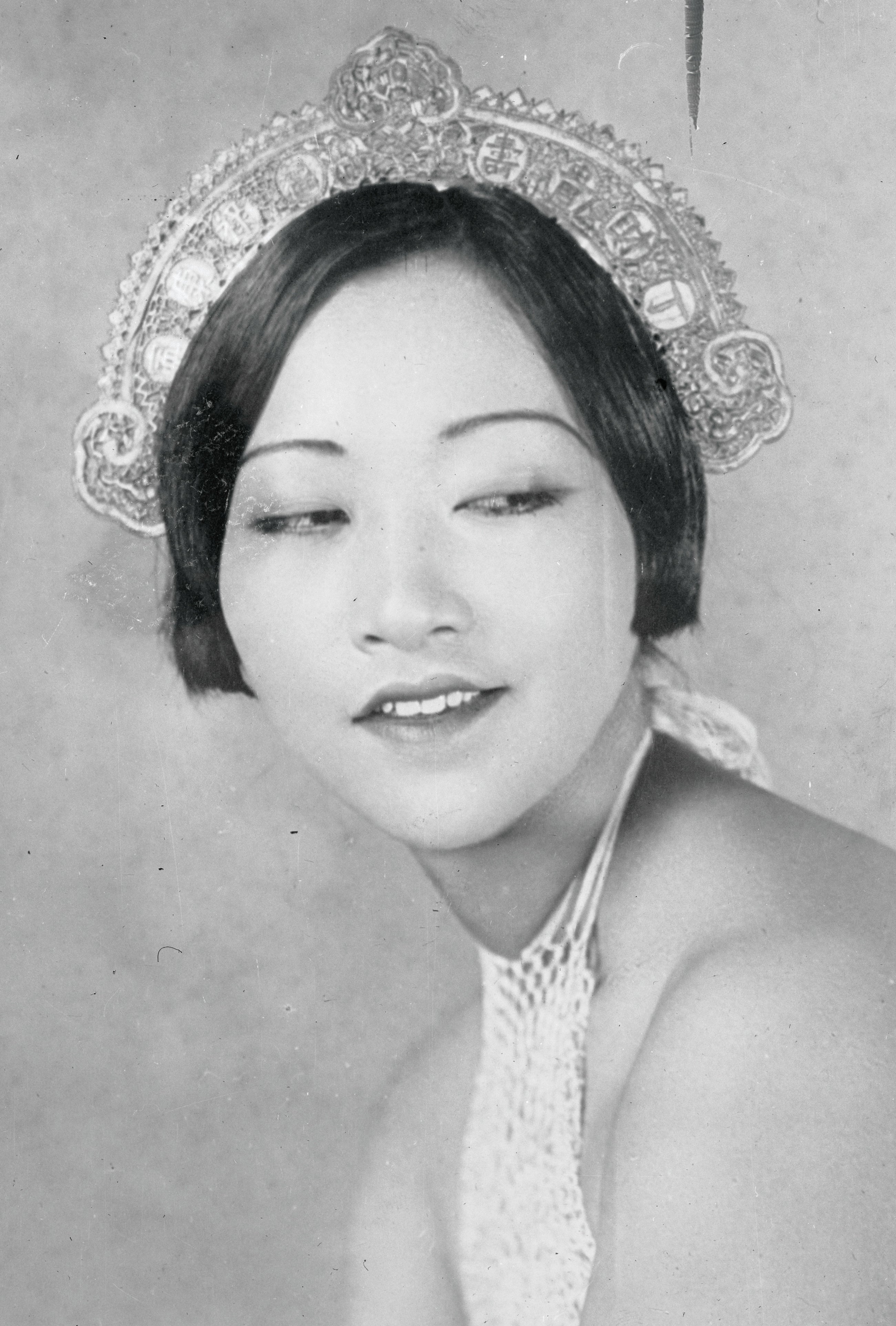 Anna May Wong smiling and looking down and left, wearing an ornate headpiece on her short dark hair