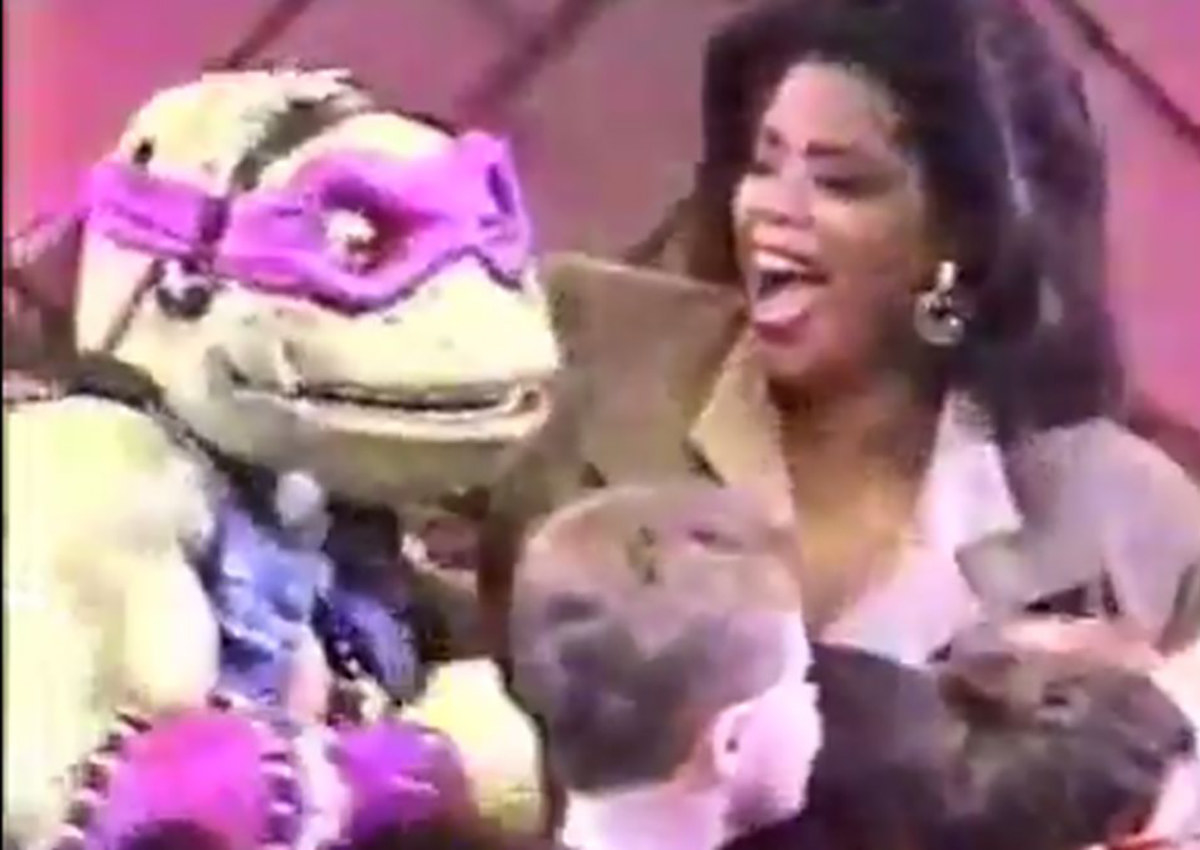 Oprah laughing as she puts her arms around a person in Donatello costume