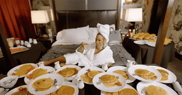 Rico Nasty on a hotel bed with a dozen plates of pancakes