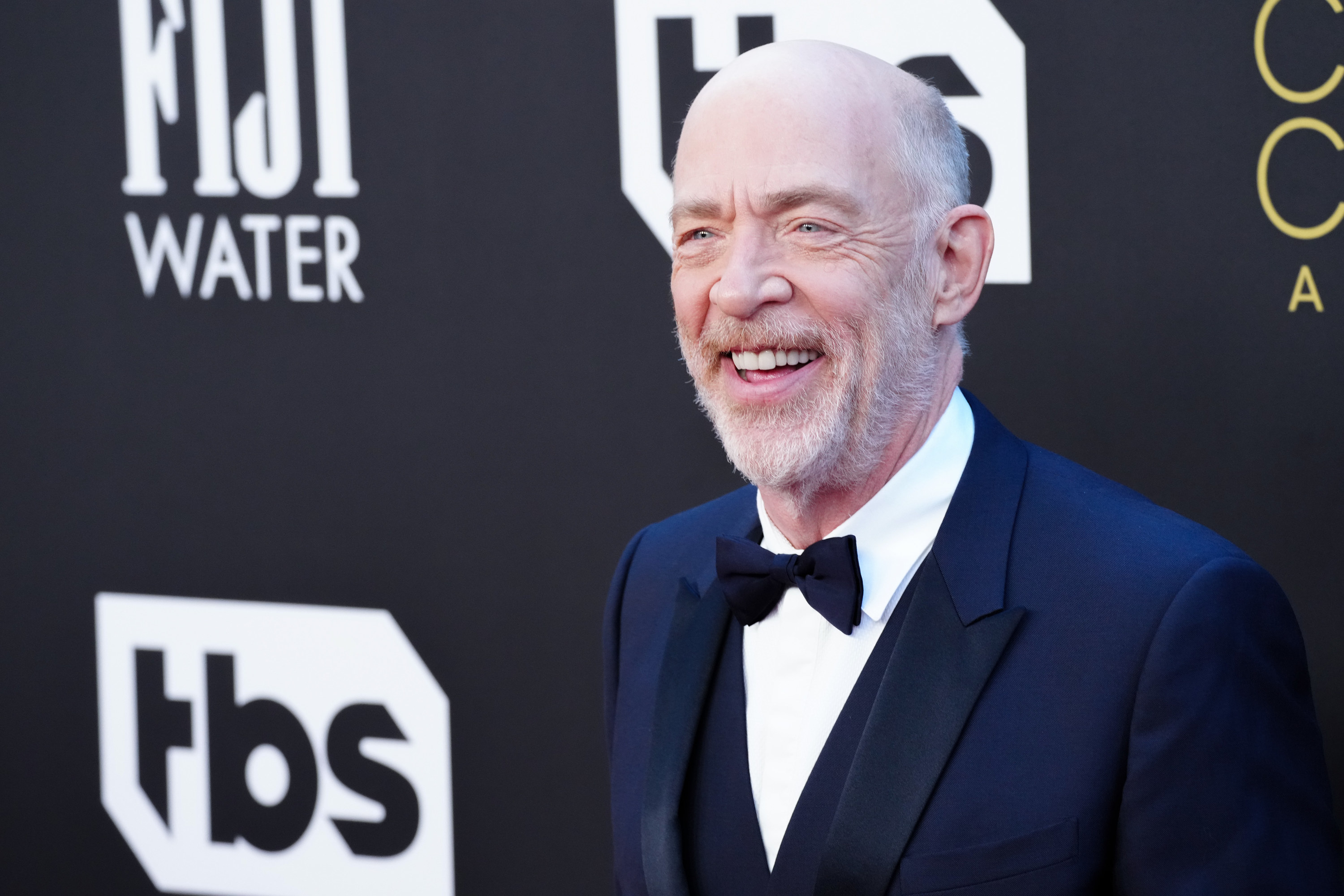 J.K. Simmons wearing a tuxedo and smiling at something off camera