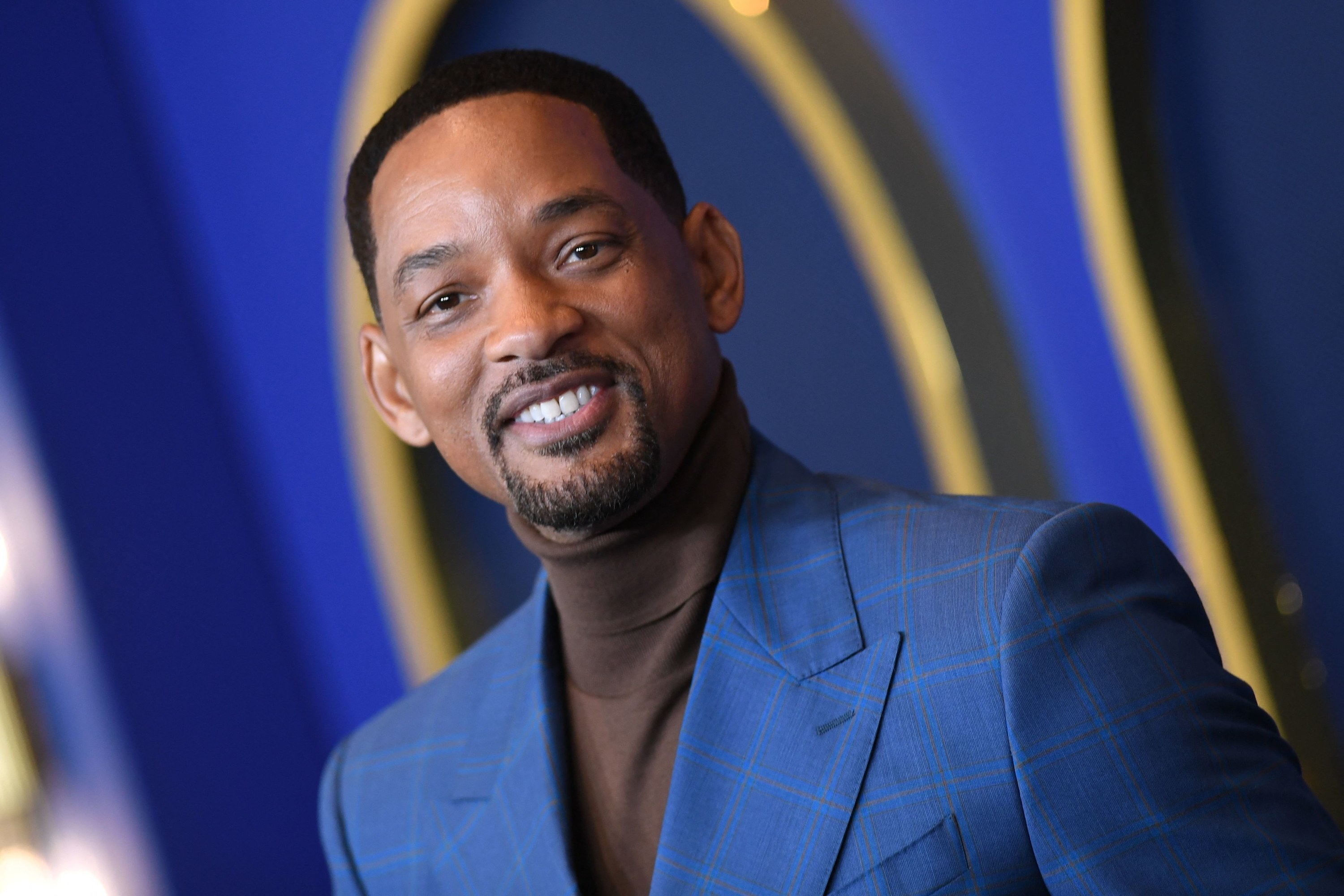 Will Smith wearing a turtleneck and suit jacket and smiling at the camera