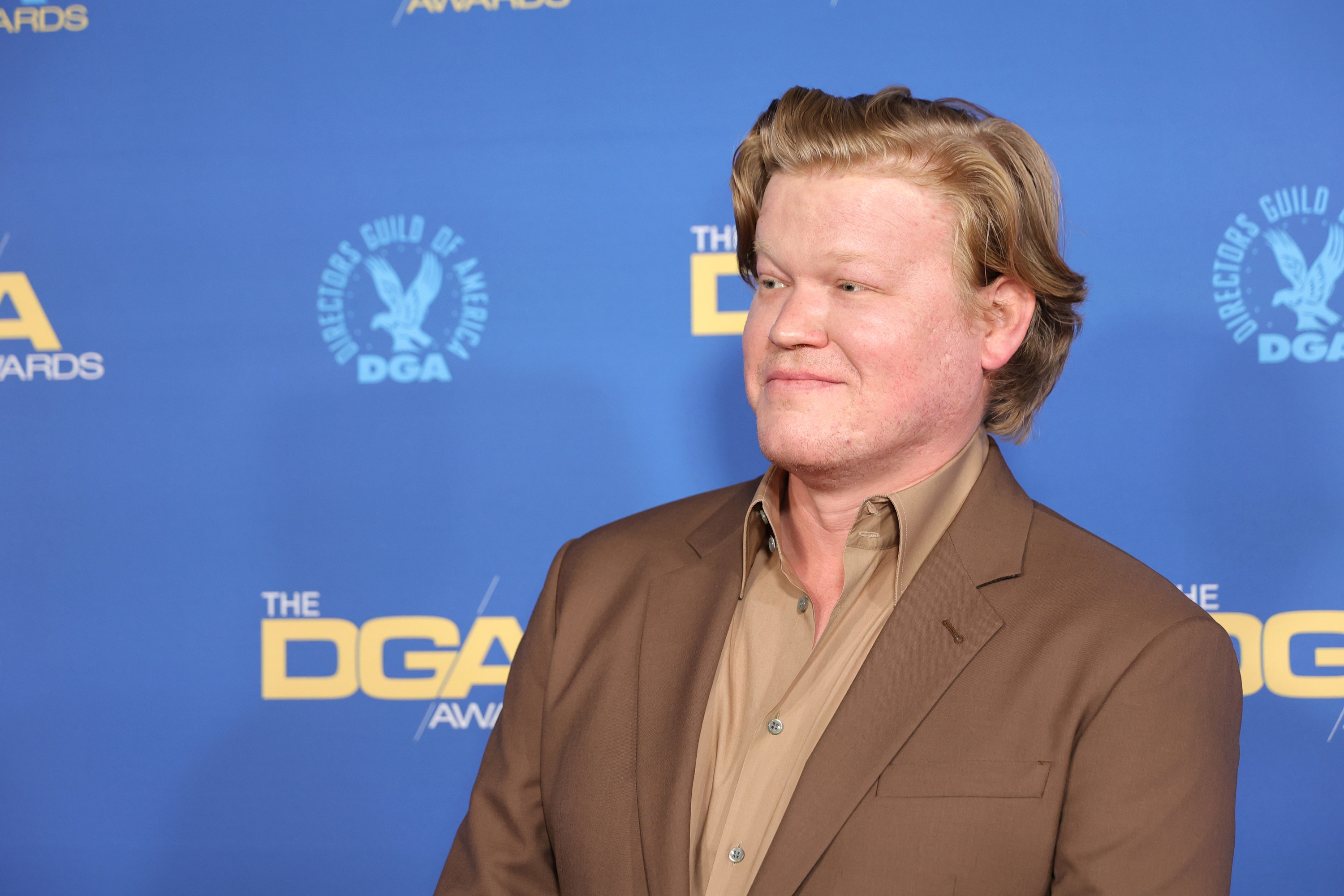 Jesse Plemons in a suit smiling at something off camera