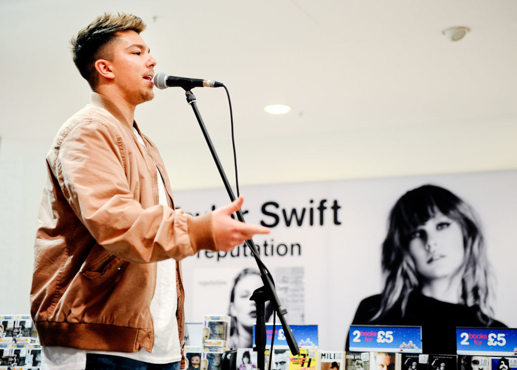 Matt Terry in a brown jacket, jeans and a white top, singing into a microphone which is on a stand