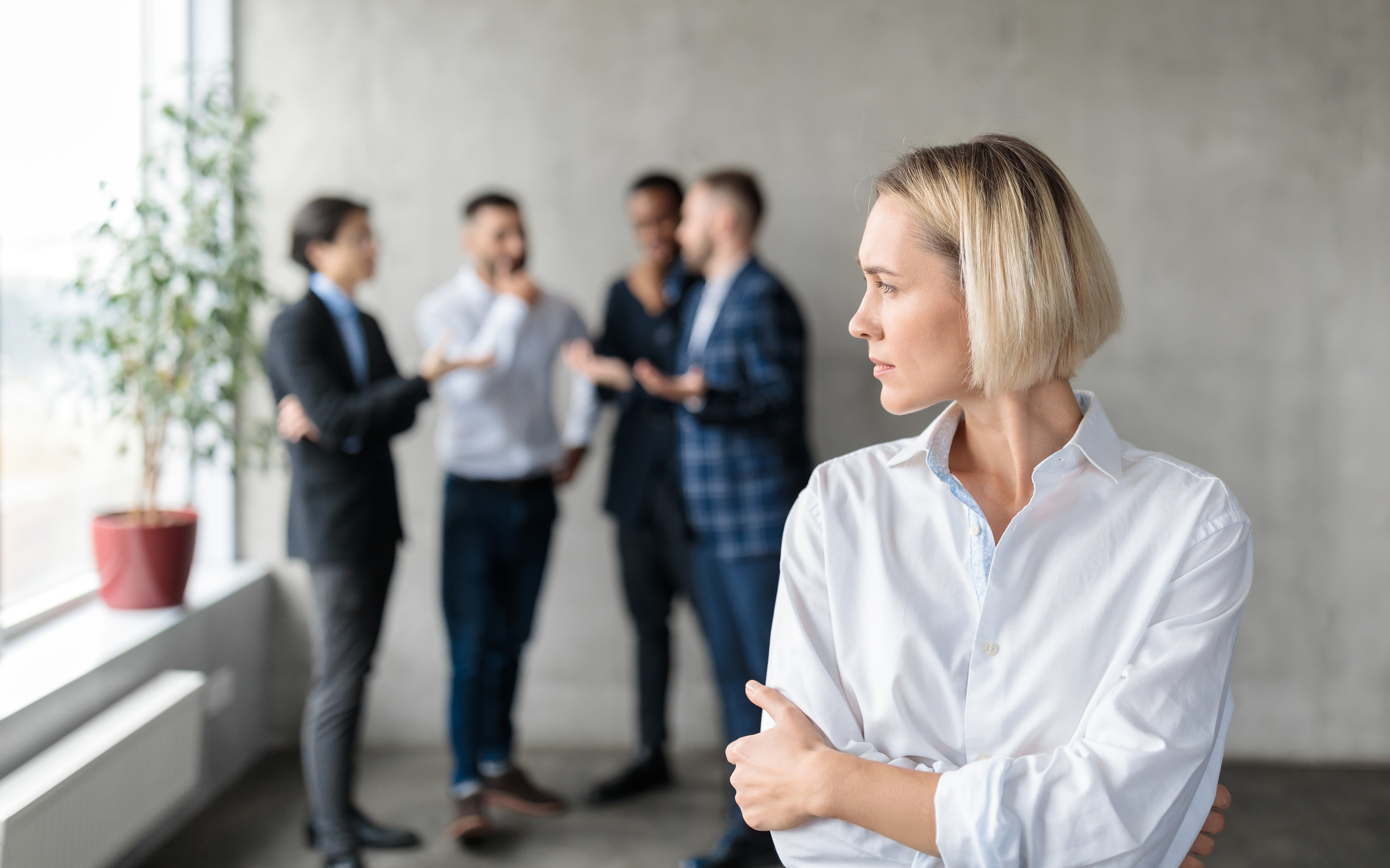 A woman looking off to the side with a group of men standing behind her talking to each other