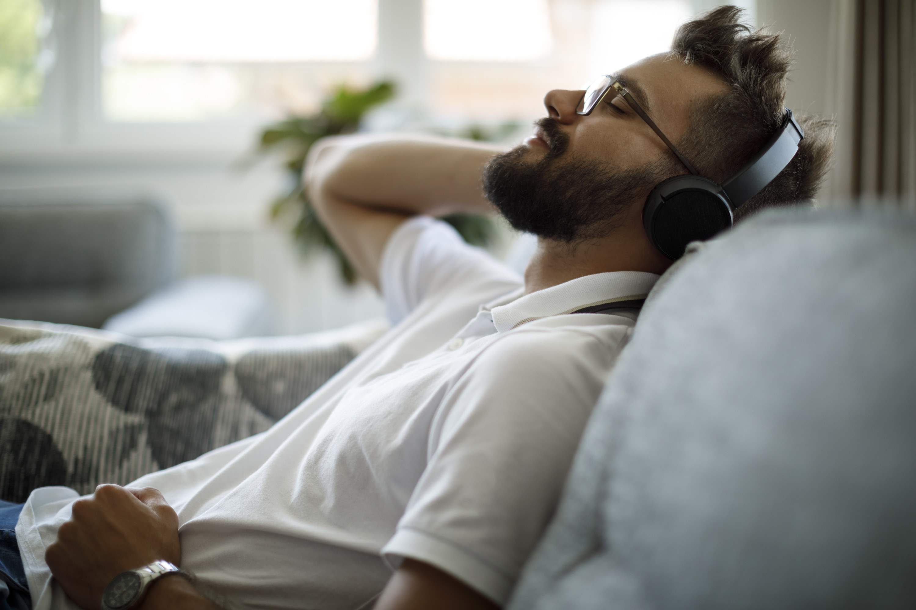 Smiling man with Bluetooth headphones relaxing on a sofa