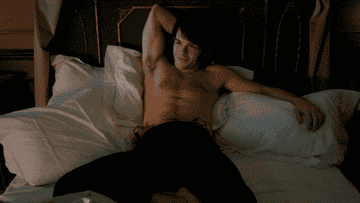 A shirtless Jonathan Bailey lies on the bed and smiles