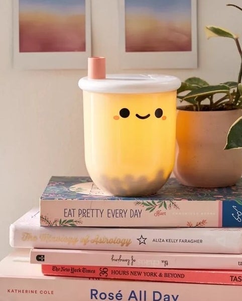 A bubble tea cup shaped lamp sitting on a stack of books in a bedroom