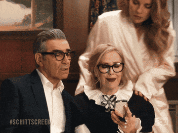 a gif from &quot;Schitt&#x27;s Creek&quot; of Johnny and Alexis looking over Moira&#x27;s shoulder while she looks at something on her cellphone