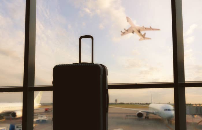Lone suitcase in front of an airport window with an airplane flying in the background outside