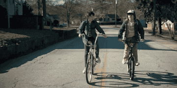 Finn Wolfhard as Mike and Gaten Matarazzo as Dustin ride bikes down the street in &quot;Stranger Things&quot;