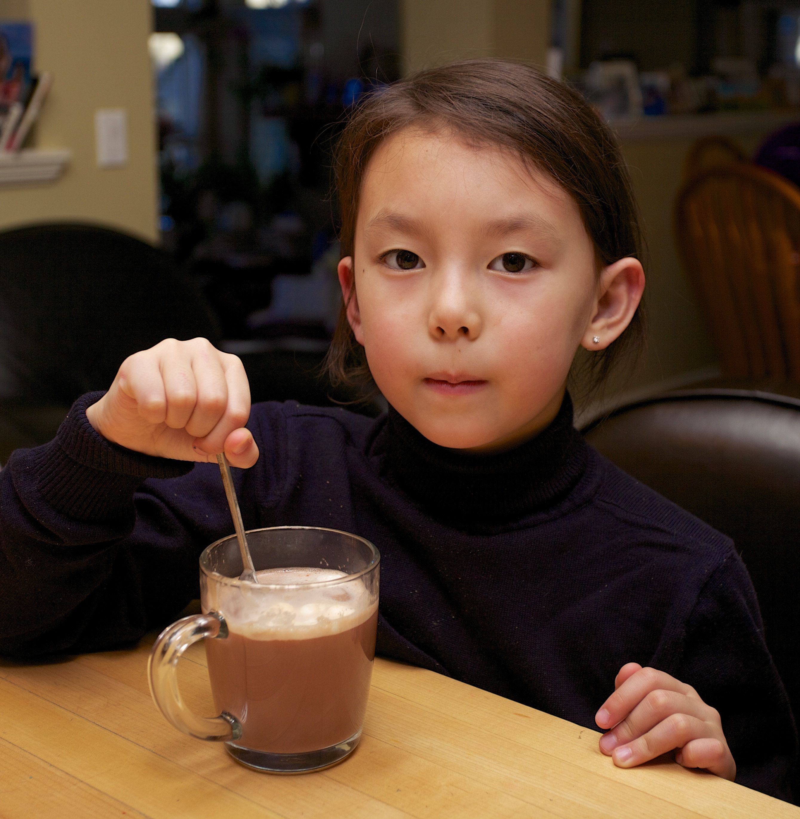 Child stares into the camera while stirring hot chocolate