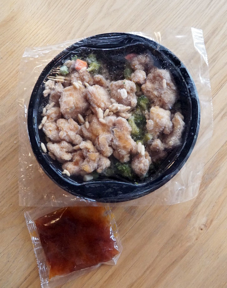 A frozen Mandarin-style orange chicken bowl with a sauce packet on the side