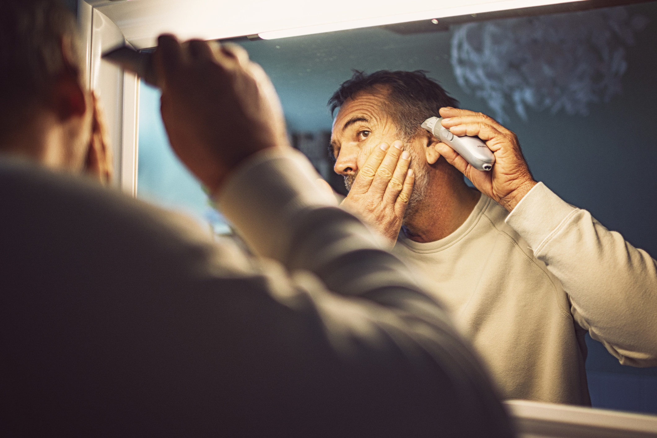 Man cutting his own hair in the mirror with a trimmer