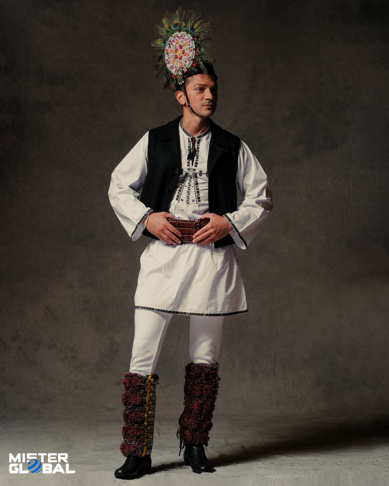 A man with a long shirt with a thick belt, vest, and headdress