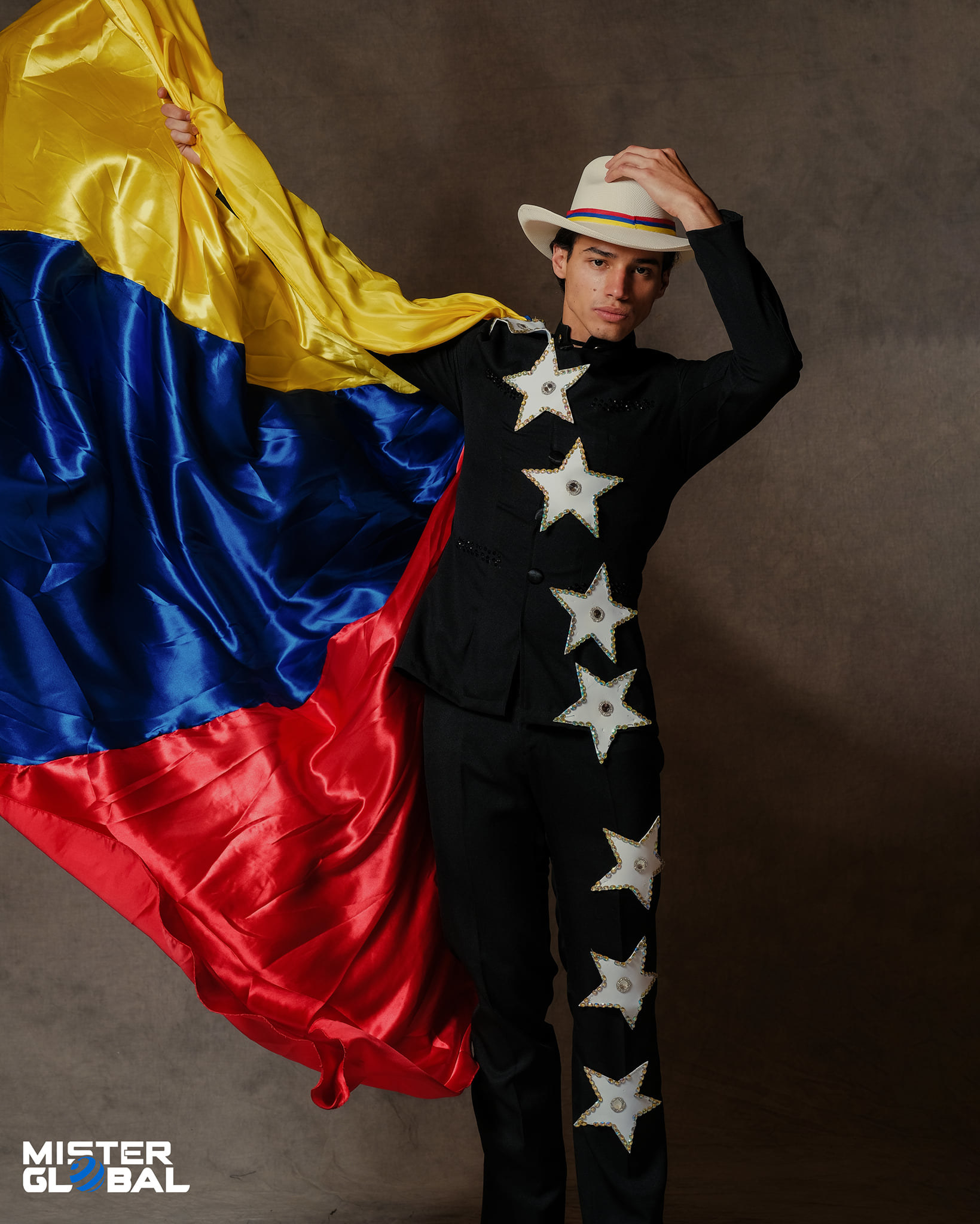 Man wearing a brimmed hat, a cape with the colors of the Venezuelan flag, and a jacket and pants with stars extending from the jacket and down one leg