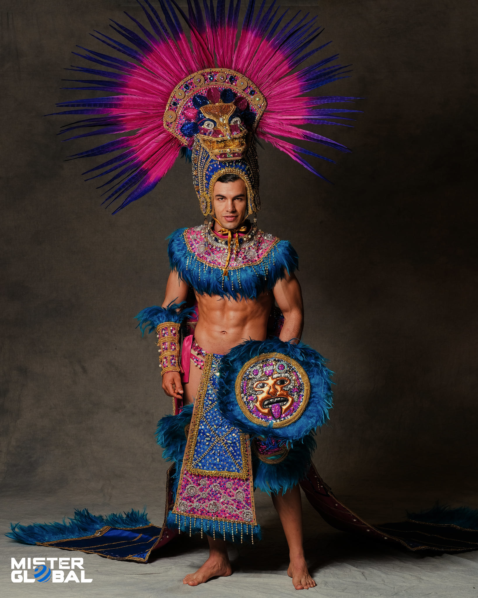 Barefoot man with ornate, feathered headdress, and ornate, chest-baring outfit