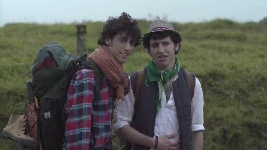 Dekel Adin as Kino carrying a backpack and Kosta Kaplan as Ra&#x27;anan staring at something, with mountains and grass in the background