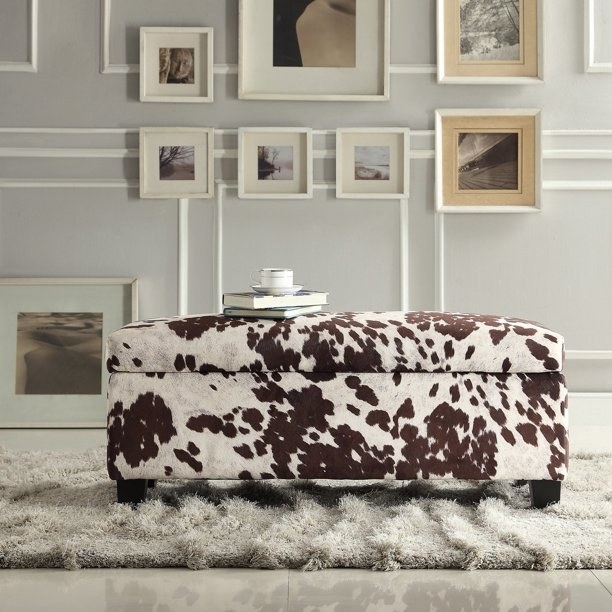 a brown cowhide bench on a rug in front of a wall with portraits hung