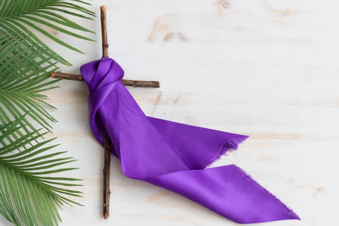 Wooden Christian cross with purple ribbon and palm leaves for lent or Palm Sunday on white wood background with copy space