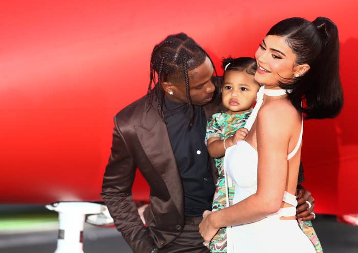 Travis leans over to look at Stormi who is being held by Kylie