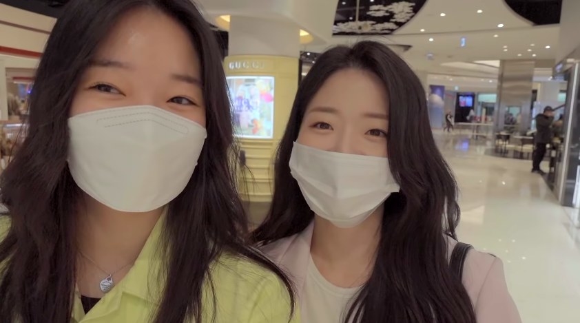 Ji-yeon poses and smiles behind masks with her sister at the mall
