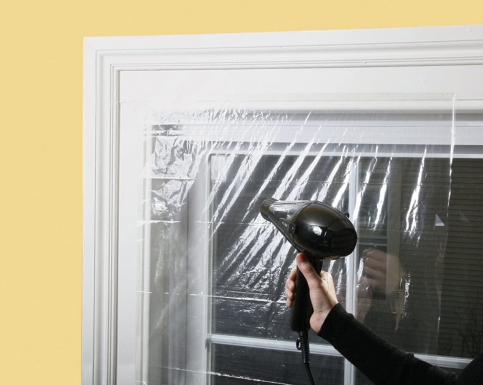 A hair dryer being used to seal the plastic wrap treatment over a window