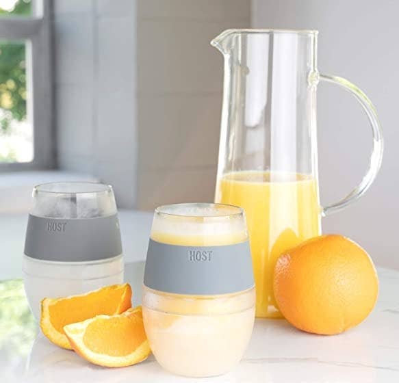 A set of glasses on a counter with a jug of orange juice and sliced orange next to them