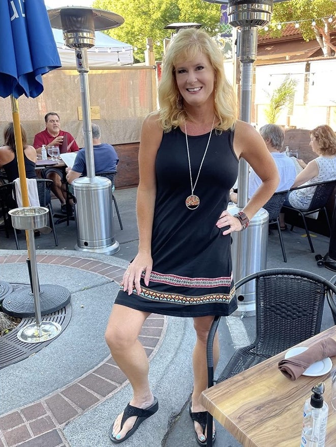 A reviewer wearing a boho sleeveless embroidered hem tank dress in black