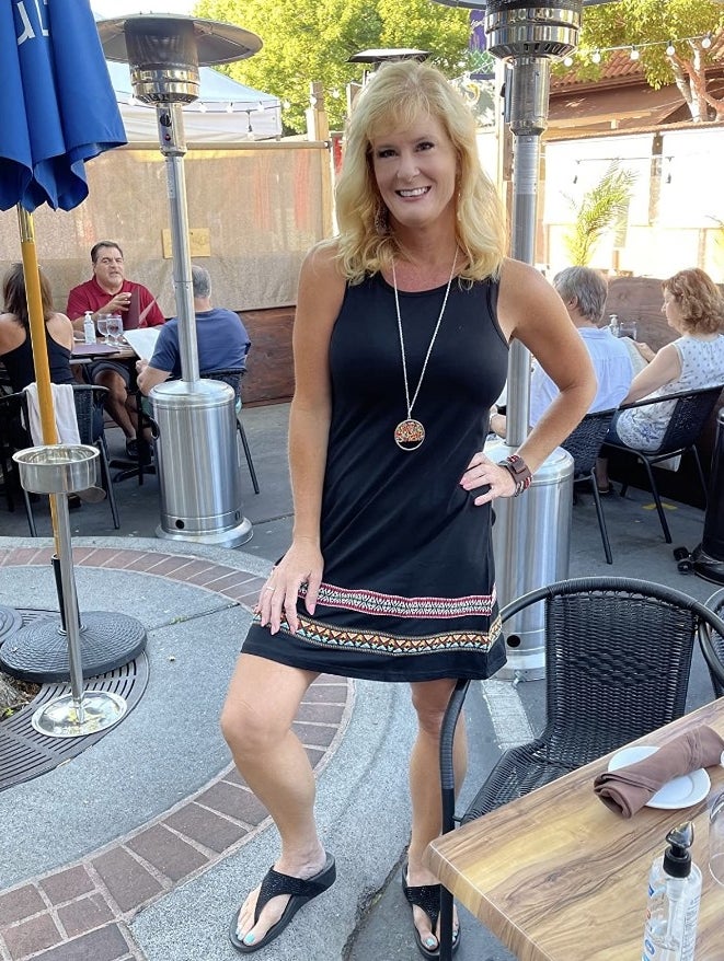 A reviewer wearing a boho sleeveless embroidered hem tank dress in black