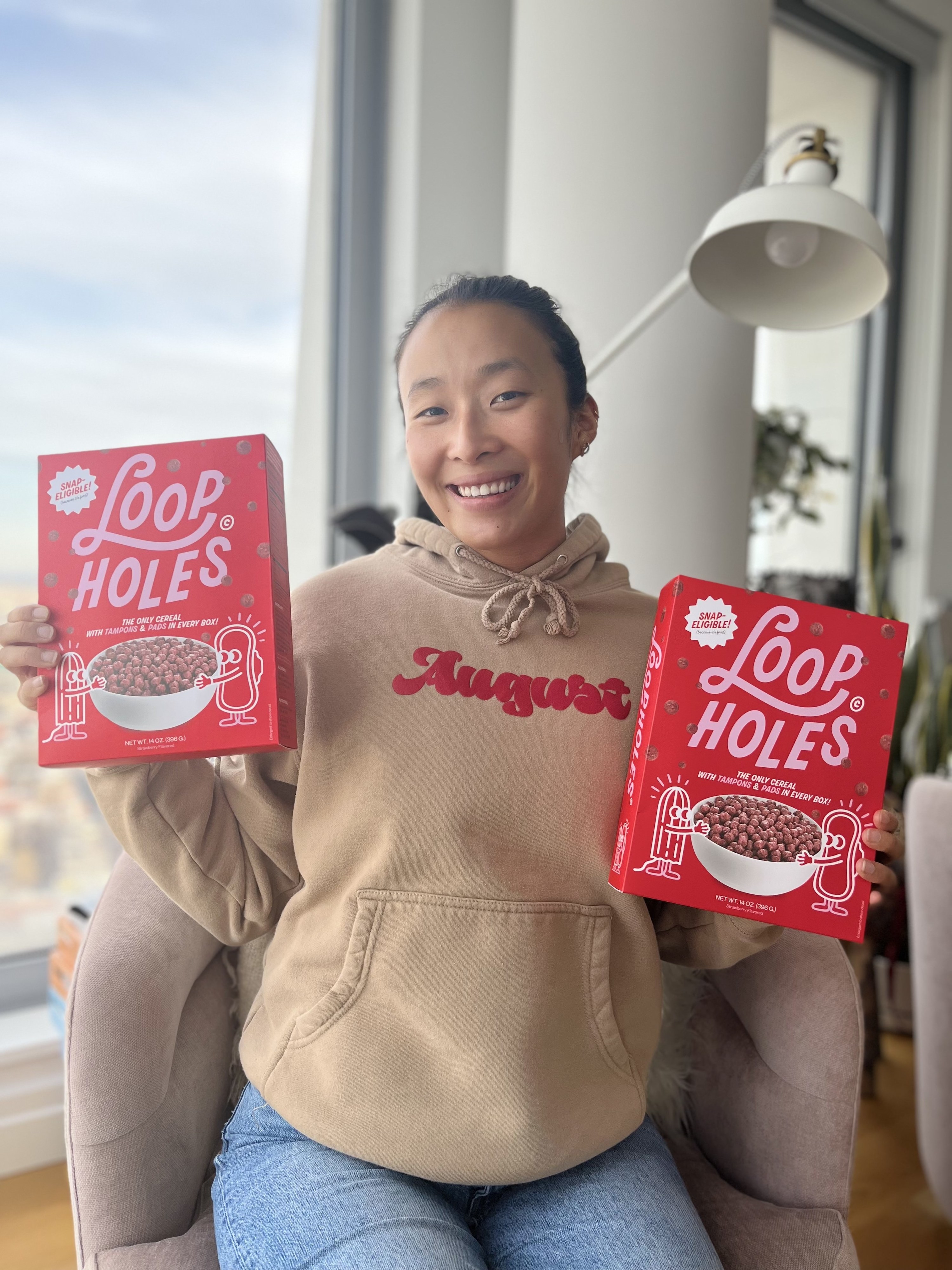 Nadya Okamoto smiling as she holds two Loophole Cereal Boxes in each hand