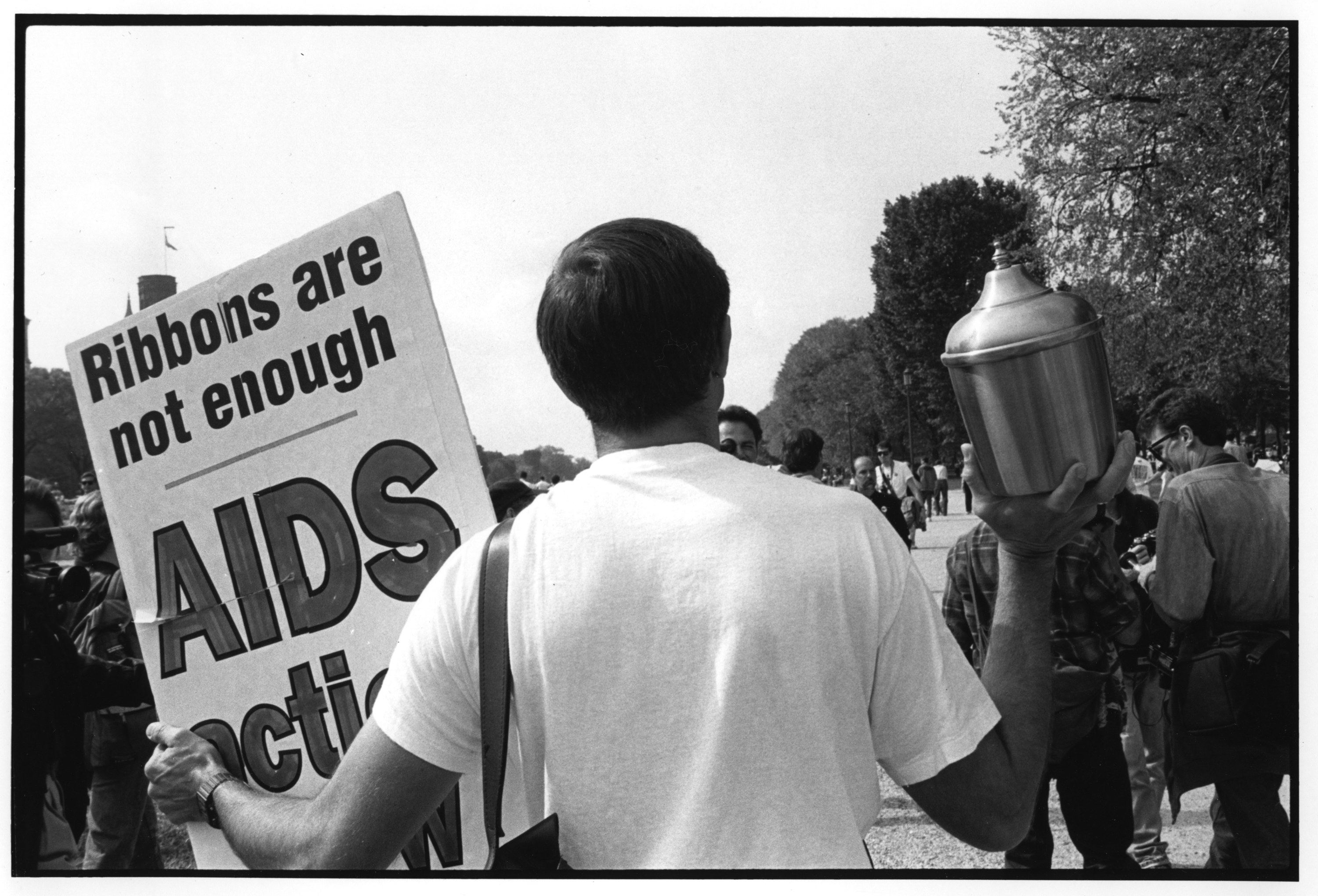 艾滋病活动家拿着一张海报,上面写着丝带是不够的和一个葬礼》与人类灰缸在示威活动中1992年11月在华盛顿特区