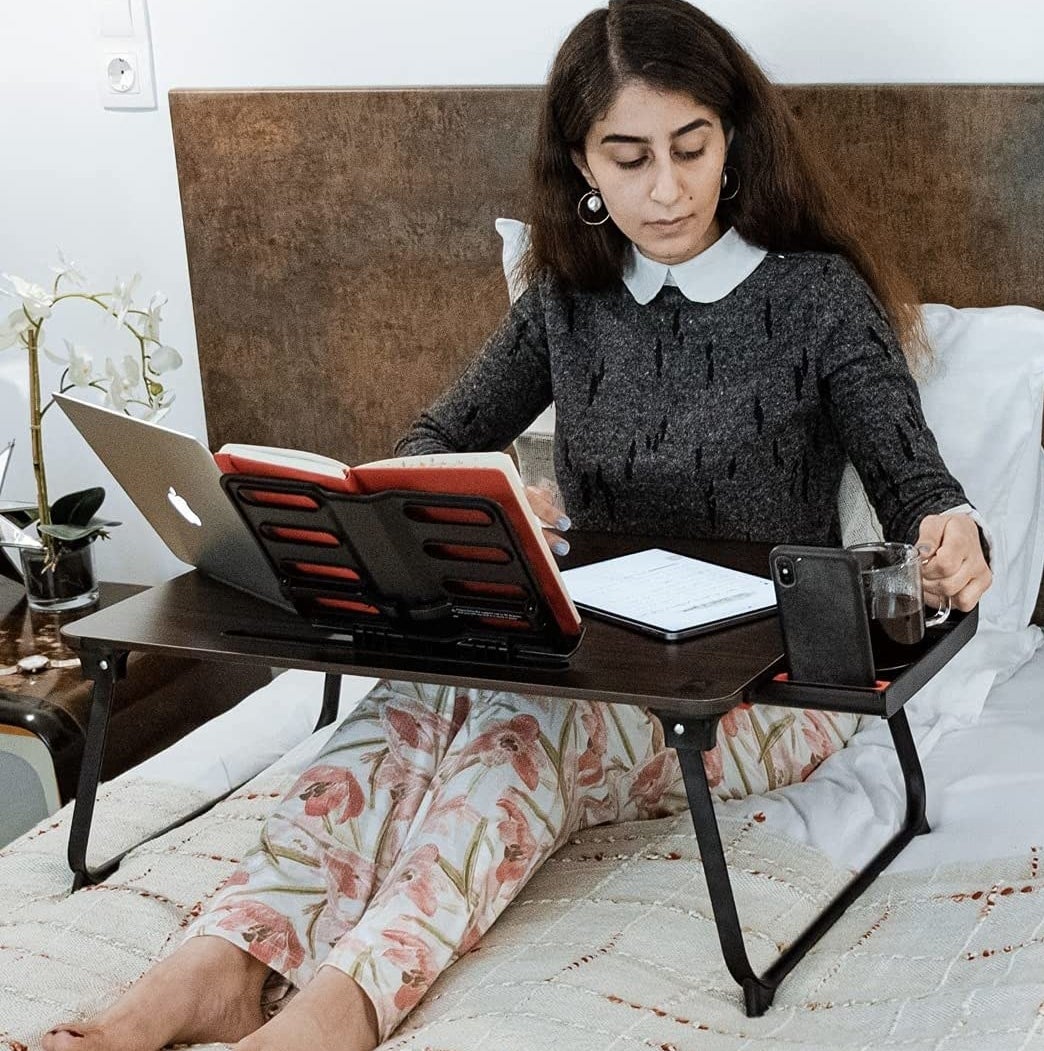 A person using the large laptop desk to work from their bed