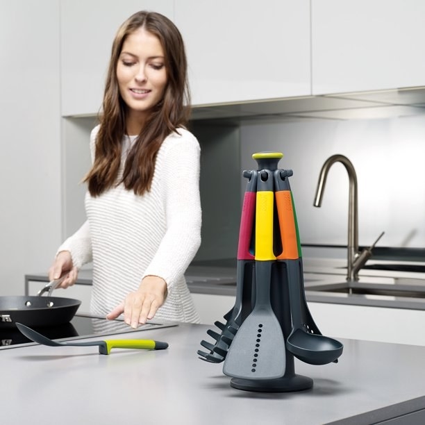 An image of a model in a kitchen next to a rotating utensil stand