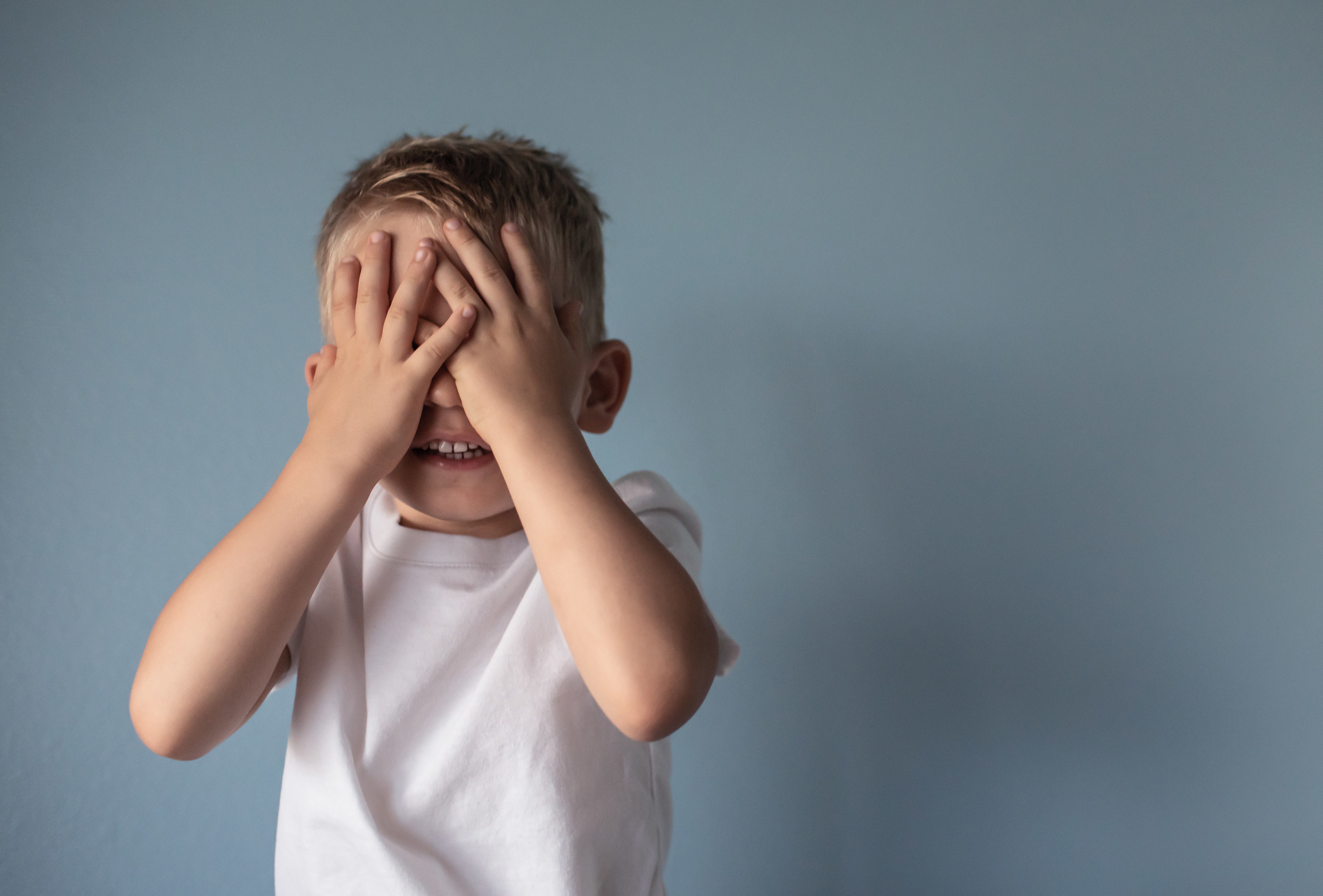 Little boy covering his eyes against gray background