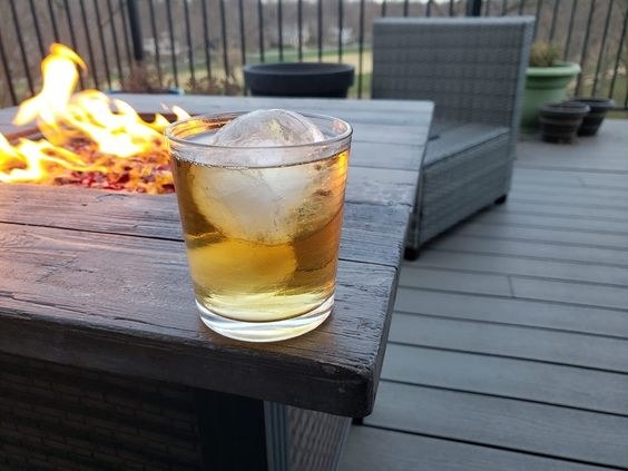 An alcoholic beverage with big ice in it on top of a fire pit