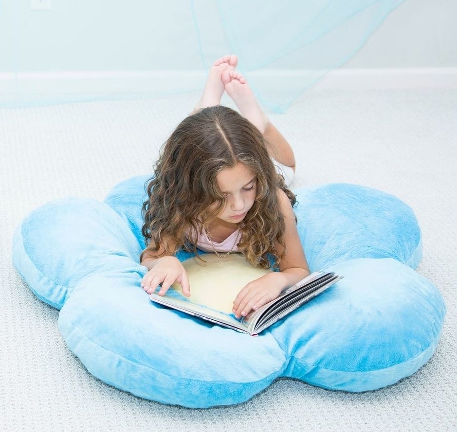 A child laying on the oversized floral shaped pillow while they read a book