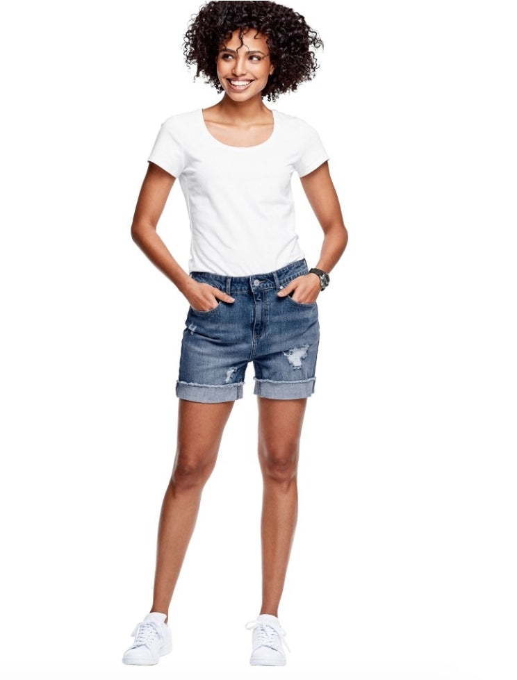 A model wearing a pair of frayed hem medium blue wash denim shorts