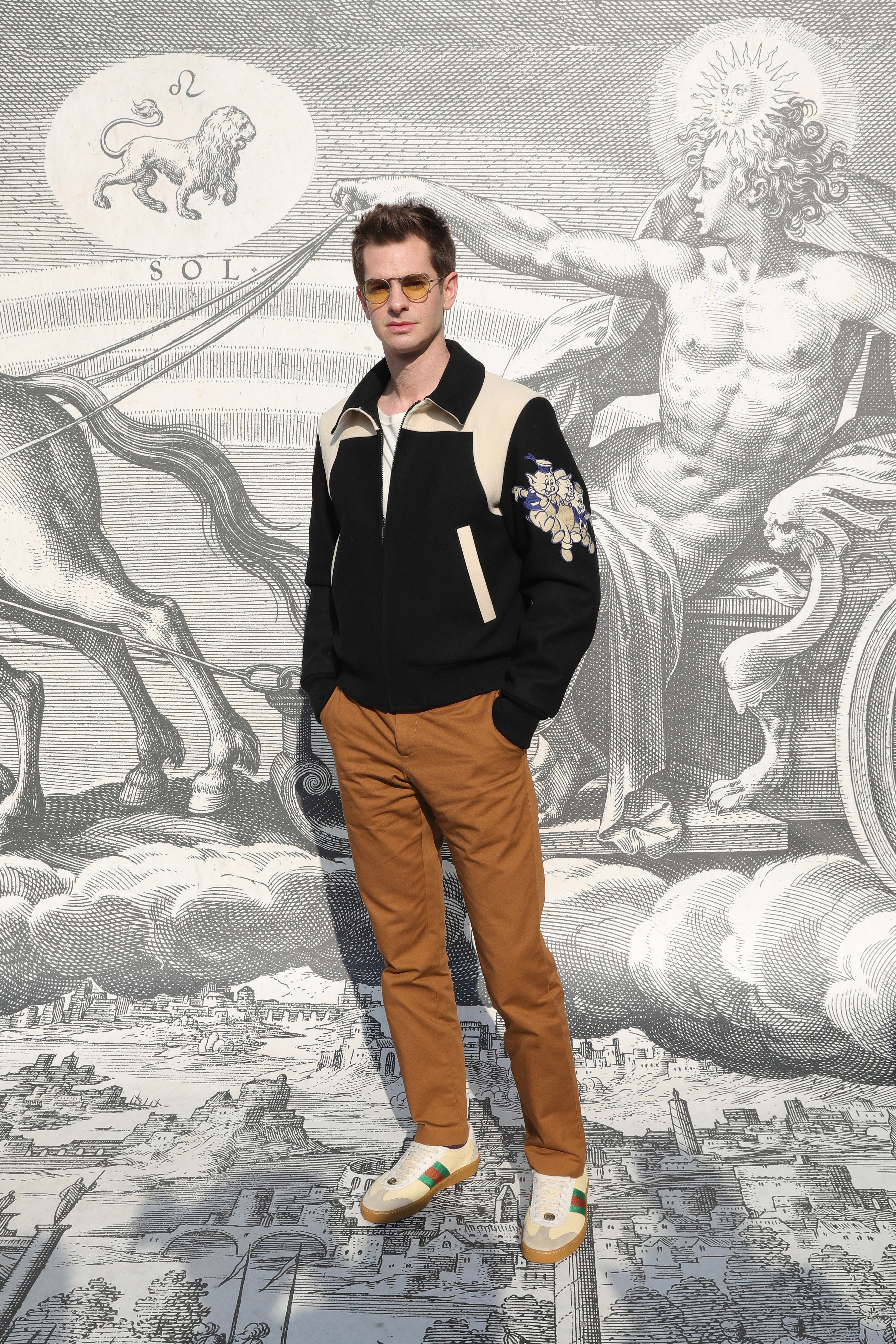 Andrew wears beige pants and a black and white bomber jacket