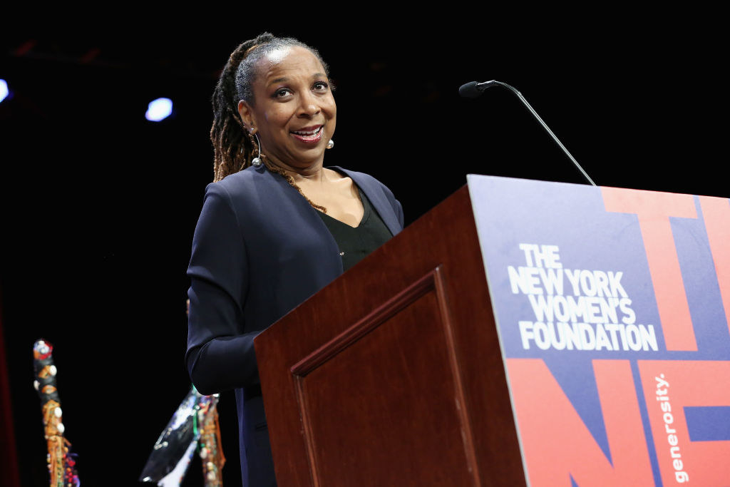 Kimberlé Crenshaw speaking at a podium with a sign on it saying &quot;The New York Women&#x27;s Foundation&quot;