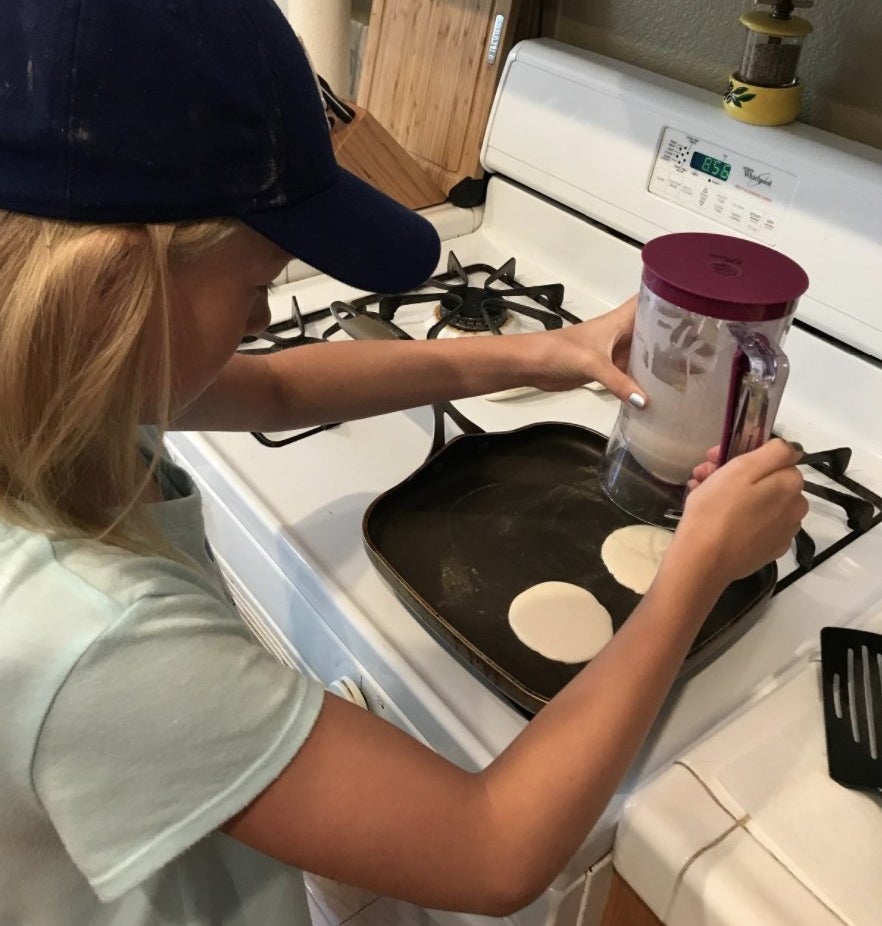Reviewer&#x27;s photo of their daughter using the pancake dispenser to make perfectly formed and mess free pancakes in the pan