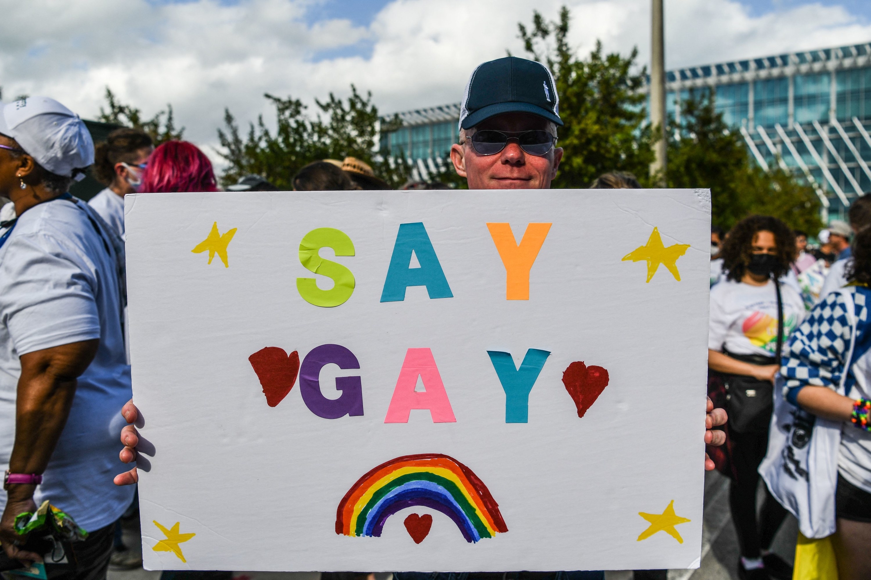 A man holding a sign that says &quot;Say Gay&quot; above a rainbow