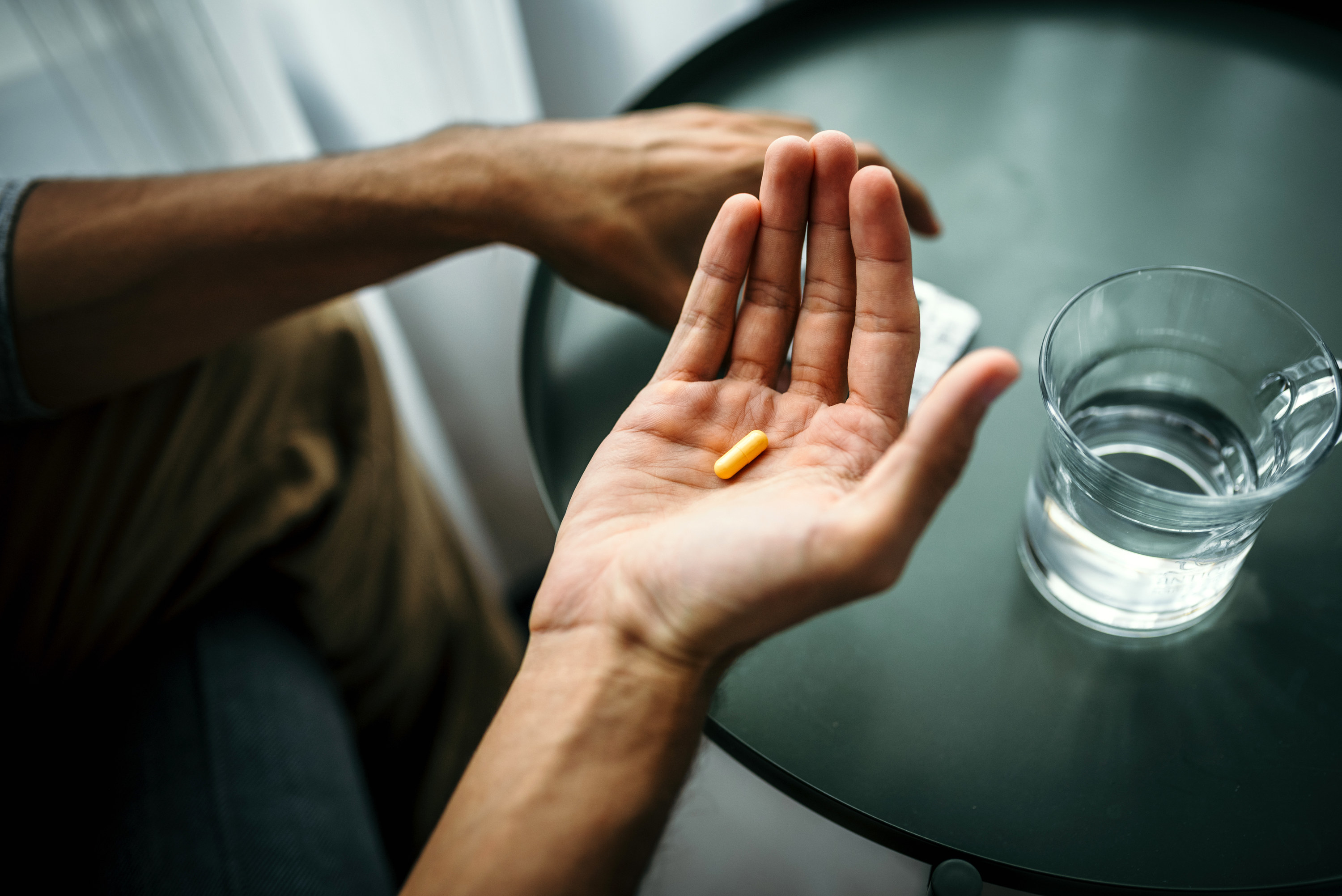 Someone holding a pill over a table with water
