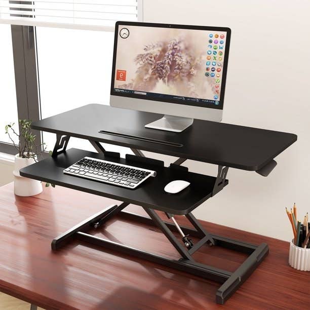 Black standing desk converter with laptop on top, keyboard and mouse on bottom shelf