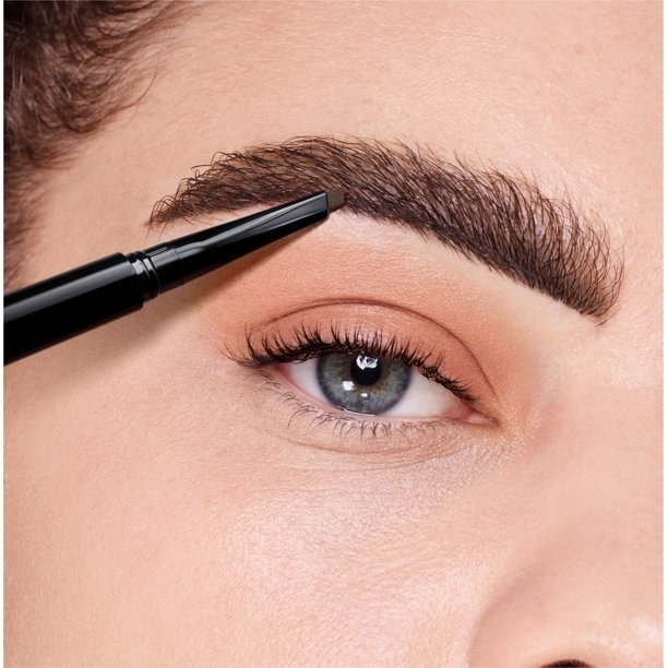 Model using brow pencil to touch up eyebrow