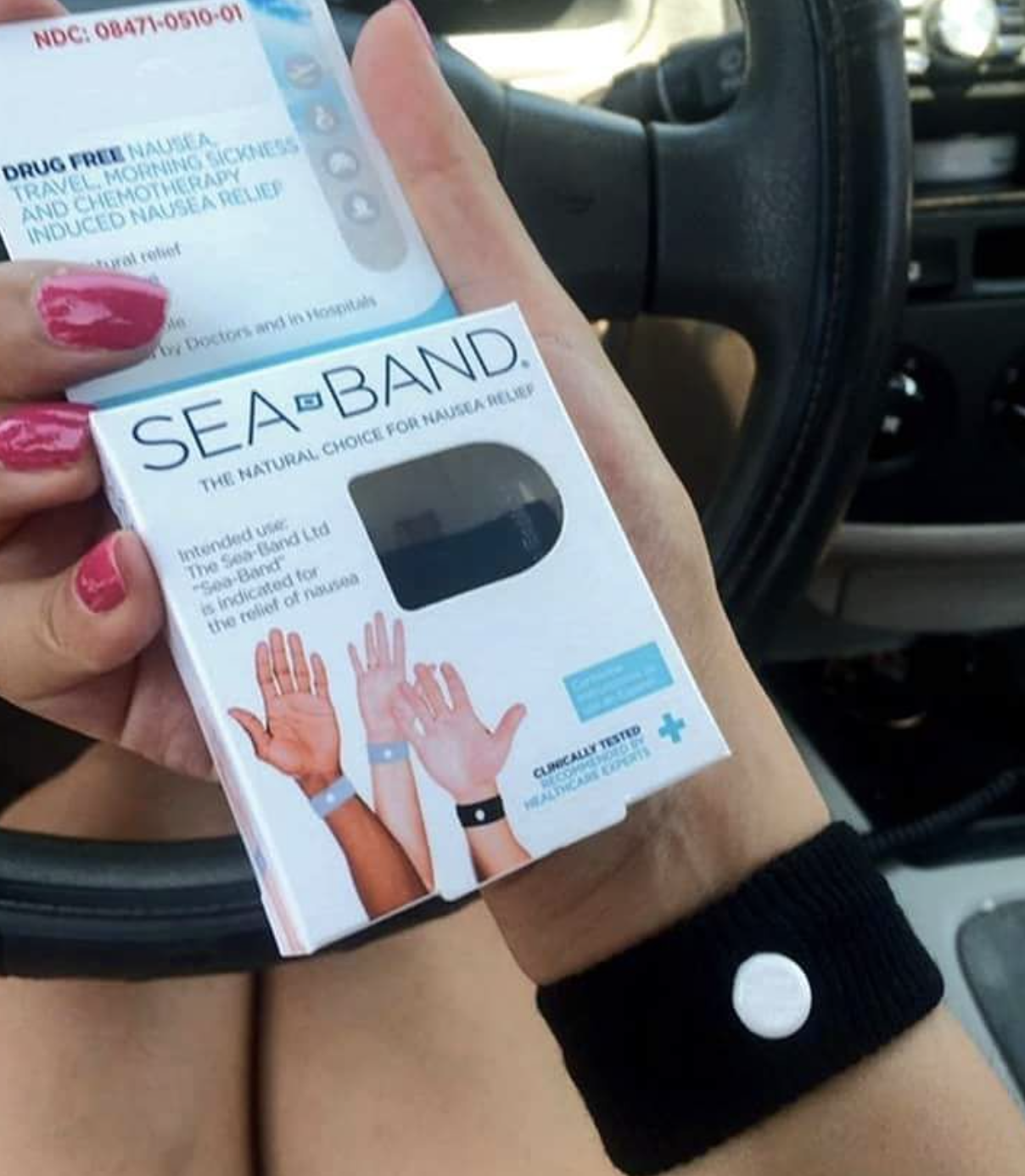 Someone wearing a Sea-band on their wrist while holding up the packaging